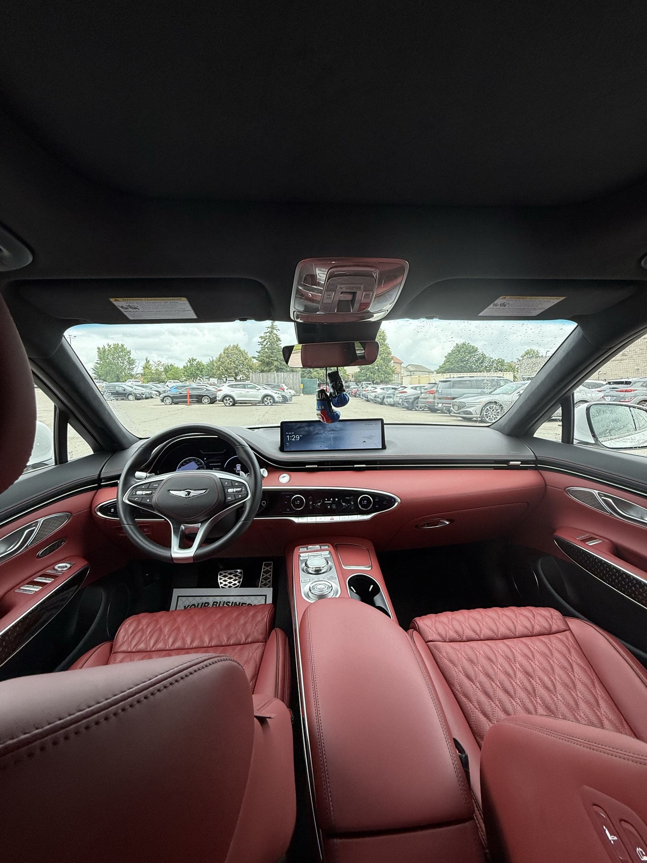 Genesis car interior with red leather seats, a wide digital display, and a parking lot view.