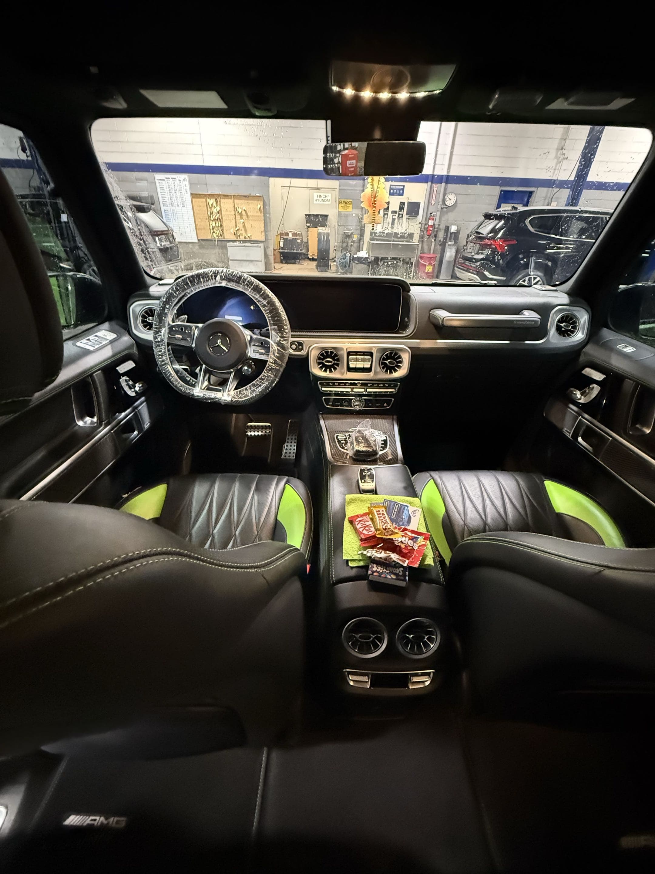 Mercedes-Benz interior with black and lime green seats, plastic-wrapped steering wheel, and snacks.